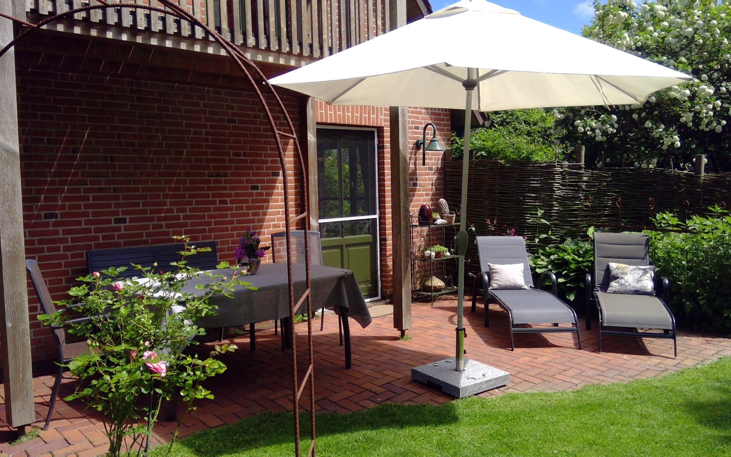 Sonnige Terrasse mit Tisch, Stühlen, zwei Liegen und Sonnenschirm.